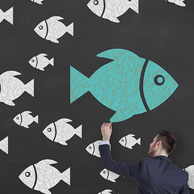 Man drawing a large fish swimming the opposite direction from other fish.