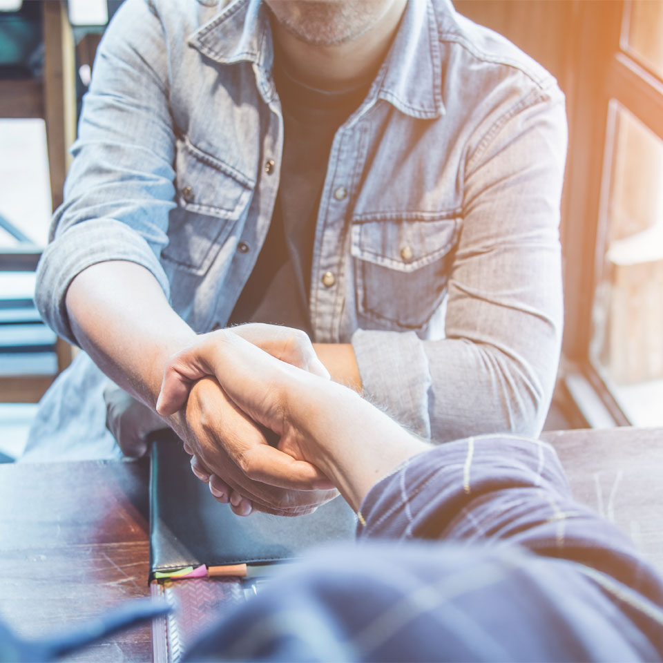 Two people shaking hands across a table, making a deal